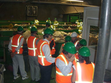 Recyclery Tour - men in orange vests, green helmets near bins